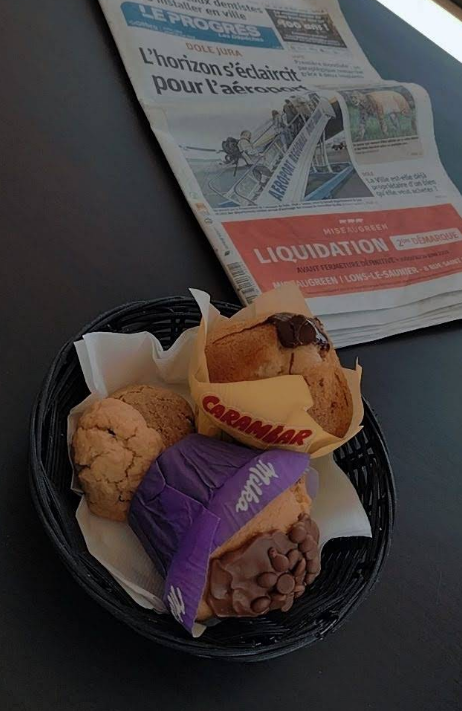Panier de muffins, cookies et viennoiseries posé sur la table avec le journal local Le Progrès